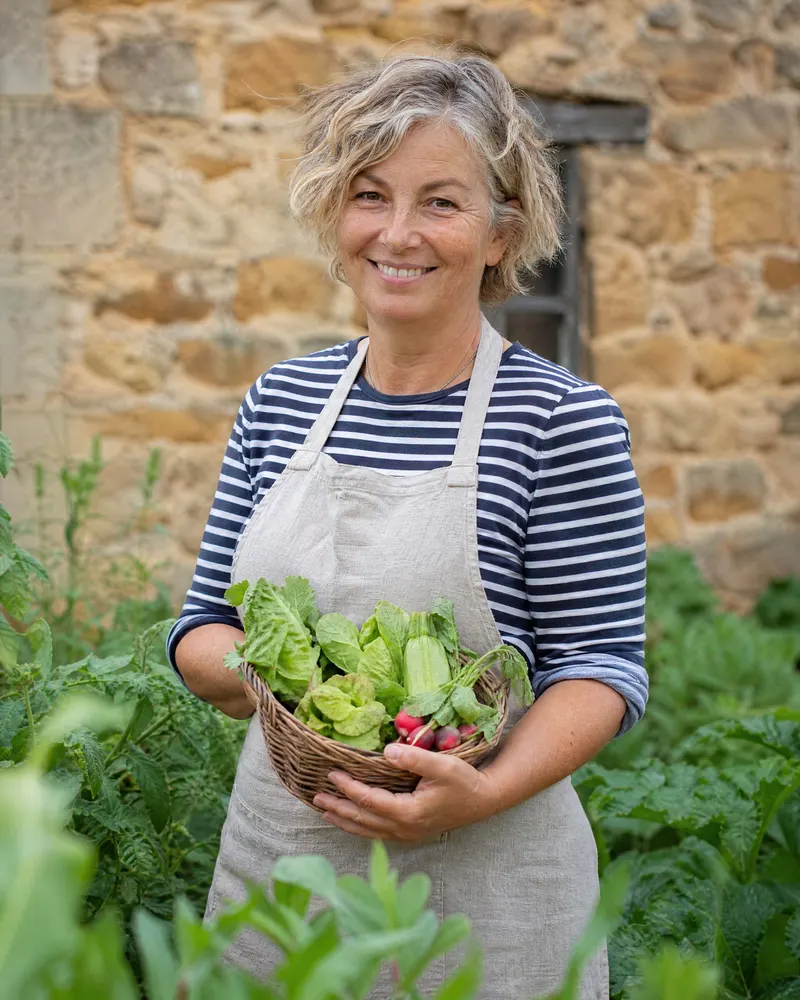 Portrait de Solène, souriante, dans le potager de la longère.